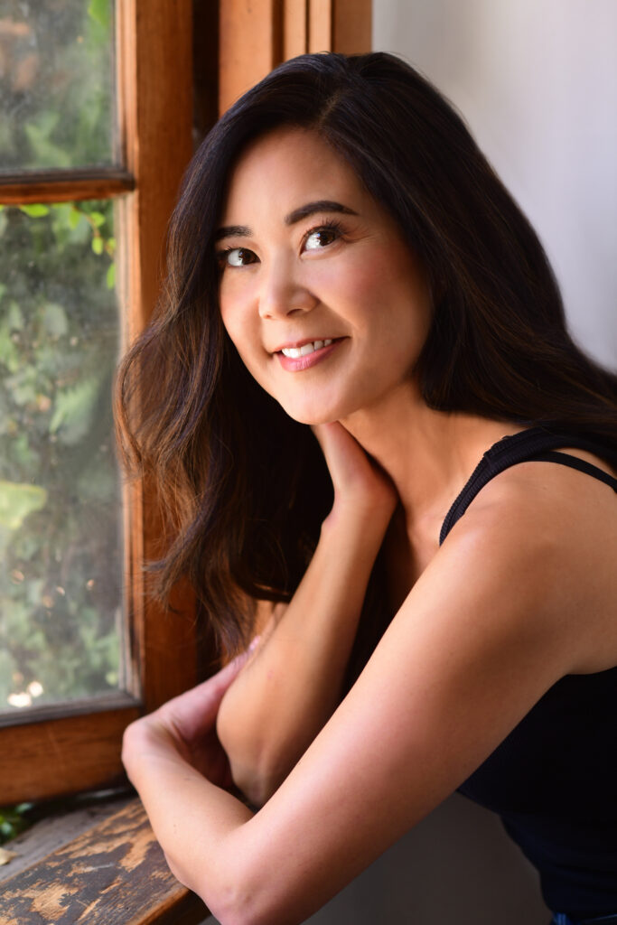 author Evelyn Skye in a black tank, smiling, leaning on windowsill